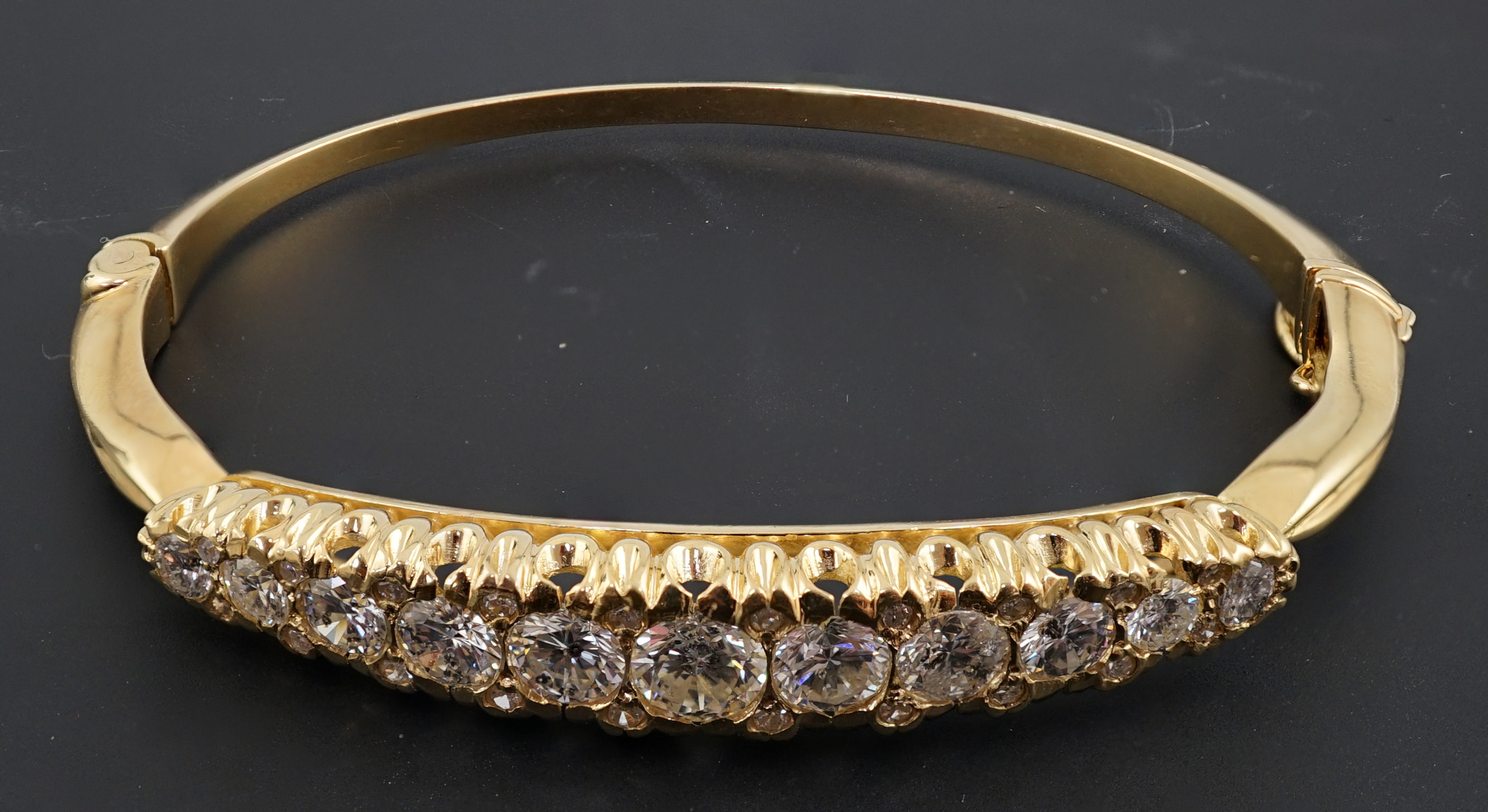 A gold and graduated eleven stone diamond set hinged bangle
